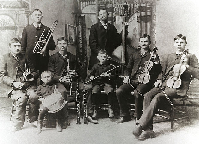 It's the historic Bach Band in Rochester with Johann Reinhold Bach as the band leader. Seven of his sons are sitting, one is standing. All have musical instruments in their hands and they are looking to the viewer without smiling.