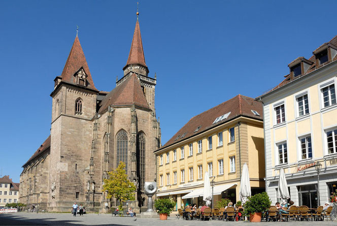 The market square in Ansbach in northern Bavaria, Germany. You can see a huge church with two towers in the left half of the picture, in the right half there are café areas in front of historic houses. Right in between, almost unrecognizable, is the silve