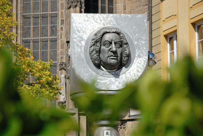 The modern silver Bach monument in Ansbach, in northern Bavaria, Germany. You can see the upper part, a cube, which is semicircular at the bottom. Light green foliage can be seen blurred in the foreground.