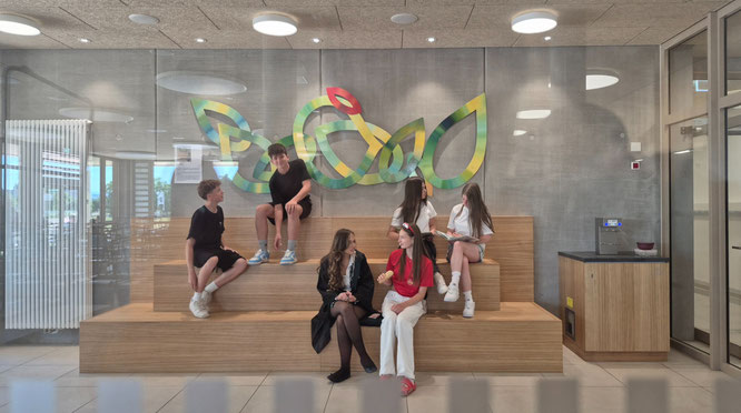 Schülerinnen und Schüler auf der Sitztreppe vor dem neuen Wandrelief 