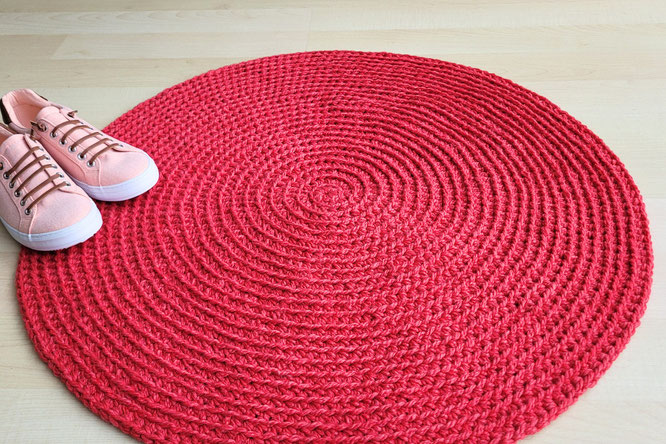 Roter runder Haekelteppich mit Spiralmuster und Turnschuhe in apricot