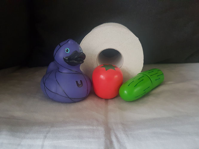 Eine violette Badeente, Spielzeug-Gemüse aus Holz und eine Rolle Toilettenpapier als Smybole für 5 typische Kleinkind-Sätze.