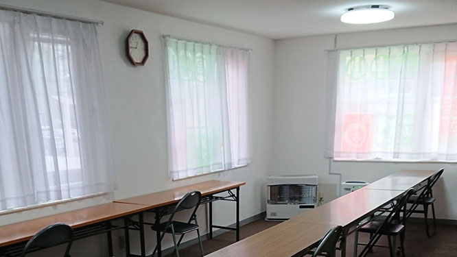 白いカーテンと木目調のデスクが並ぶ、清潔で明るい学習塾の教室風景