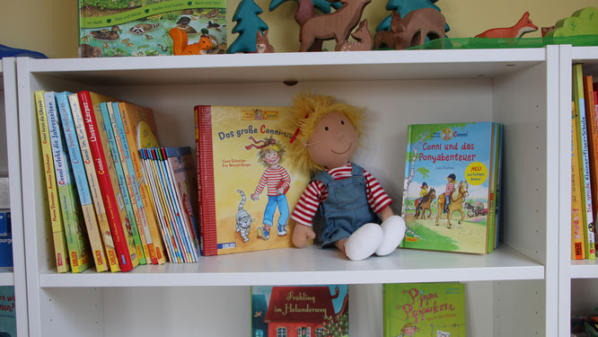 Conni-Puppe sitzt im Bücherregeal mit vielen Conni-Büchern