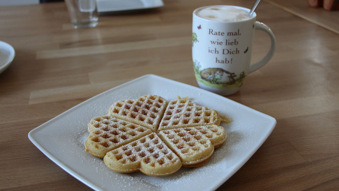 Eine Waffel mit Puderzucker auf einem Teller und dazu eine Tasse Kaffee