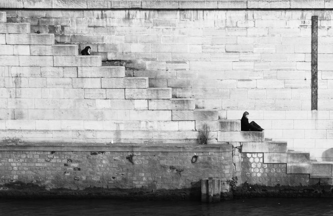 Frauen, die auf einer Treppe sitzen und in großem Abstand etwas lesen.