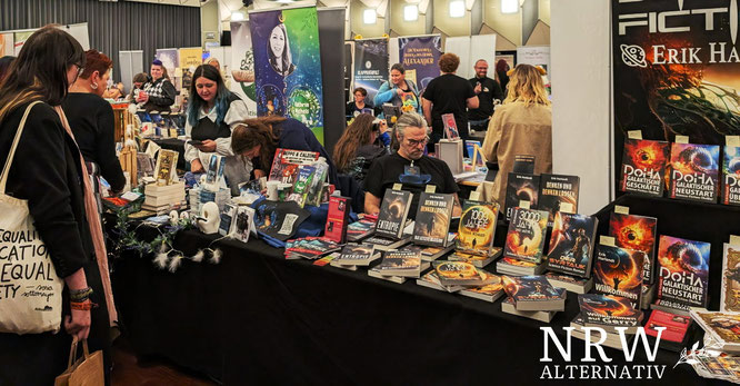 Mann hinter Büchertisch mit Science-Fiction-Büchern, davor interessiert schauende Frauen.