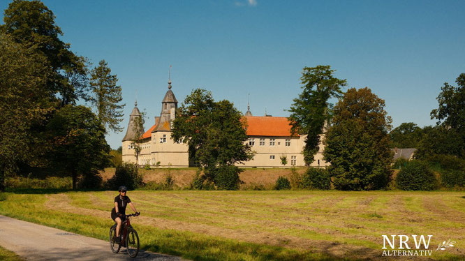 Frau auf dem Fahrrad, im Hintergrund ein Schloss. 