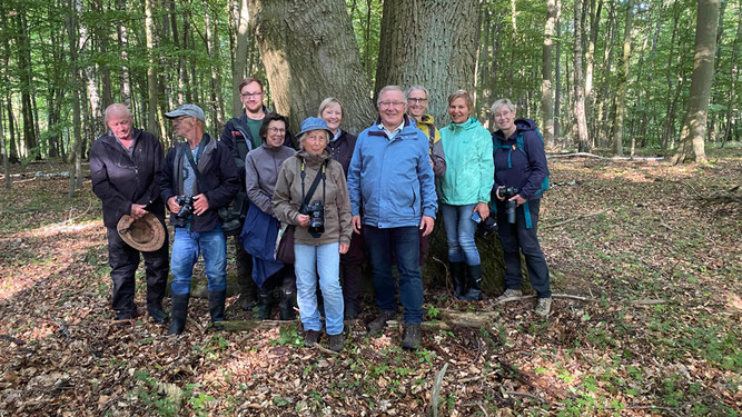 Zehn Frauen und Männer stehen für ein Gruppenbild vor 2 alten Eichen. Alle lächeln in der Nachmittagssonne mitten im Wald.