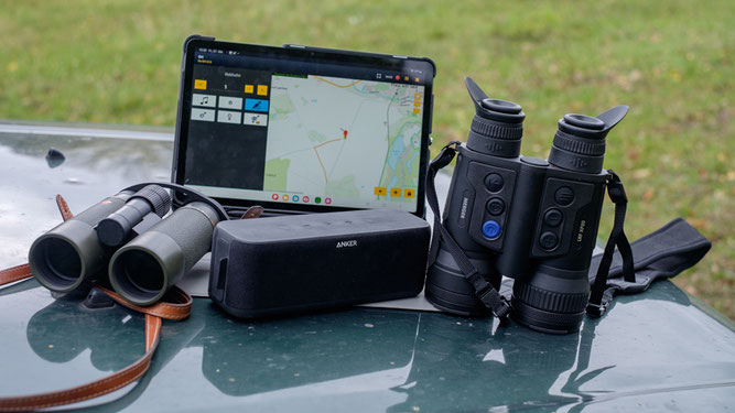 Auf einer Motorhaube liegen ein Fernglas und ein Lautsprecher. Neben einem Wärmebildglas steht ein Tablet mit einer Kartierstrecke auf dem Bildschirm.