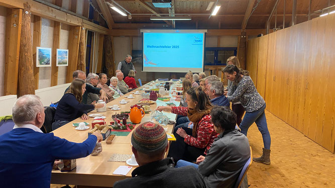 Ungefähr 25 Männer und Frauen sitzen an einem weihnachtlich gedeckten Tisch und warten auf den Beginn der Veranstaltung.