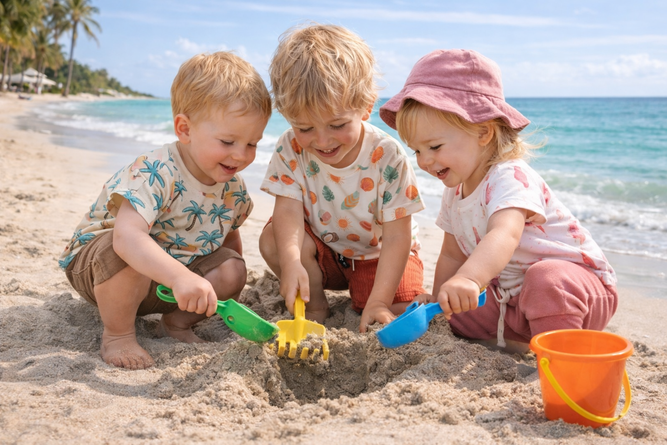 Drei Kinder spielen im Sand am Strand mit Schaufeln und Eimer - Strand Kids Sommer Kollektion | Scherzinger-Baby