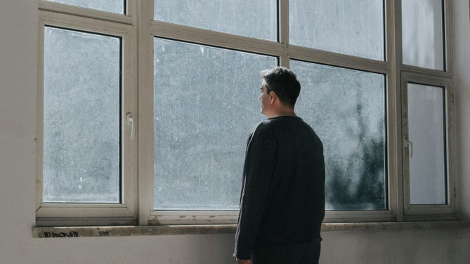 Mann steht allein am Fenster und blickt nach draussen – Symbolbild für Radikalisierung und gesellschaftliche Isolation.