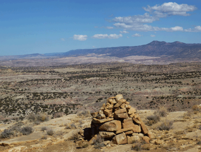 The cairn at the high point on Mesa Bernalillito. In the middle distance are badlands of the Ojito Wilderness. On the horizon is Nacimiento Ridge.