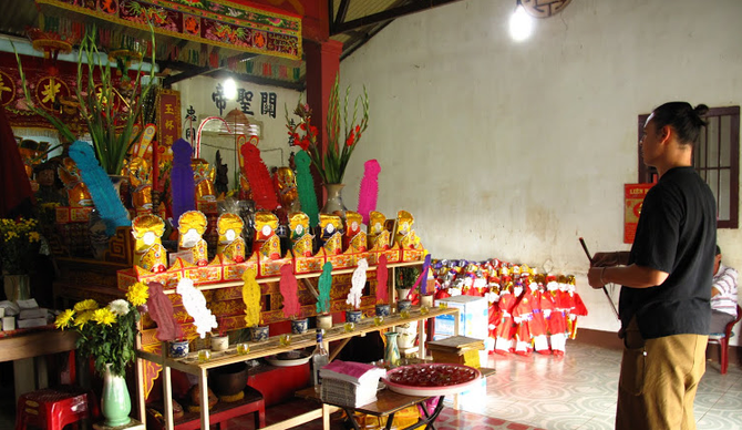 2011. COMMEMORATION DES ANCÊTRES à TUNG NGHIA. MATTHEW AVEC UN BÂTON D'ENCENS, PRIANT DEVANT L'AUTEL CENTRAL DEBORDANT D' OFFRANDES.