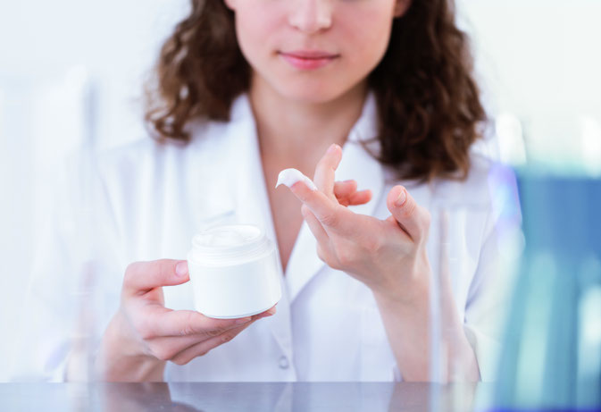 Frau im Labor hat Probe von der Sebum Plus Aubaucreme auf dem Finger.