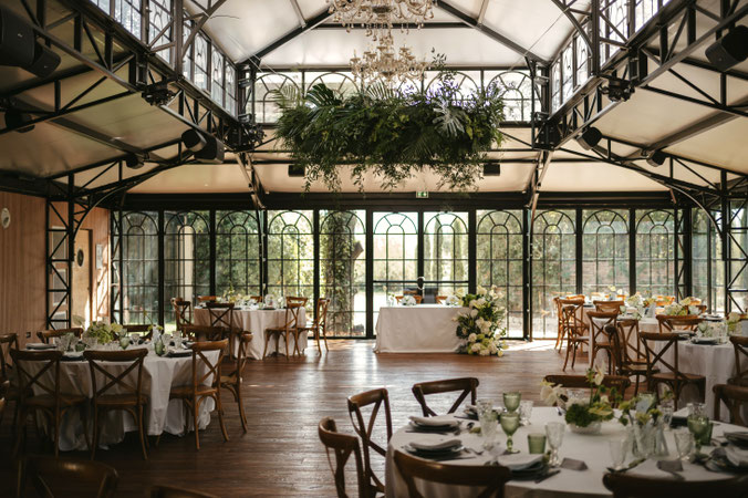 Décoration de mariage à Paris dans une verrière avec tables rondes, fleurs blanches et suspension végétale