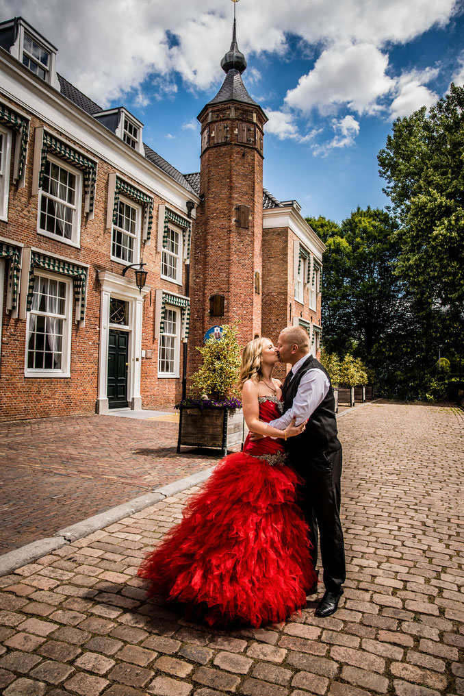 Fotoshoot buiten koppel zoenend met mooie rode jurk voor mooi gebouw 