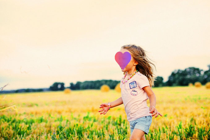 Ein Mädchen läuft lachend über ein Feld. Das Gesicht ist mit einem Herzchen überdeckt. Ein Symbol für eine schöne Kindheit und positive Glaubenssätze..Schematherapie und Psychotherapie in Gladbeck