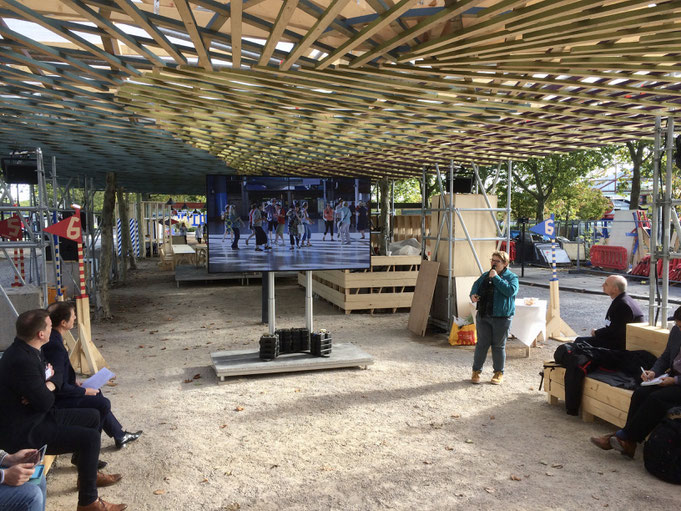 Monica Ferguson bei der Präsentation auf der offenen Festival-Bühne. Die temporäre Struktur zwischen Einkaufszentren und Bushaltestelle zieht immer wieder auch neugierige Passanten an.