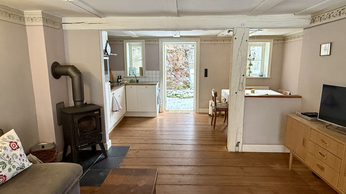 Wohnzimmer mit Kamin und Klavier sowie Küche mit Blick in den Garten
