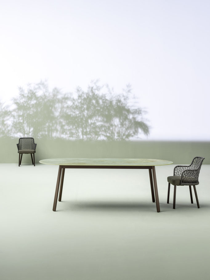 Tavolo da esterno con sedie outdoor in ambiente minimal con sfondo verde e atmosfera raffinata.