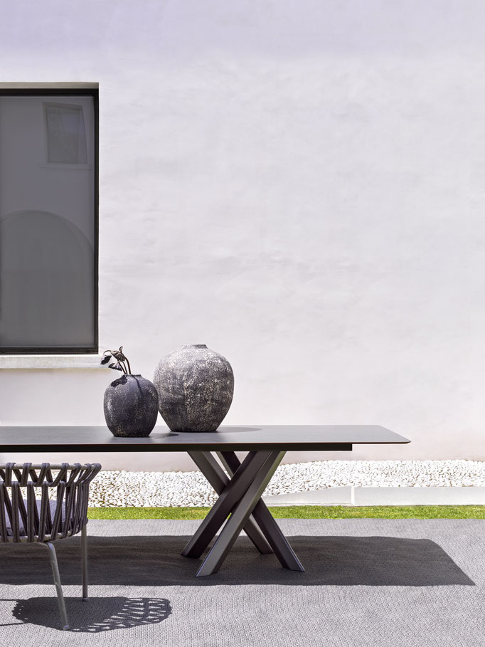 Tavolo da esterno con struttura scura, piano rettangolare e dettagli decorativi su terrazza moderna.