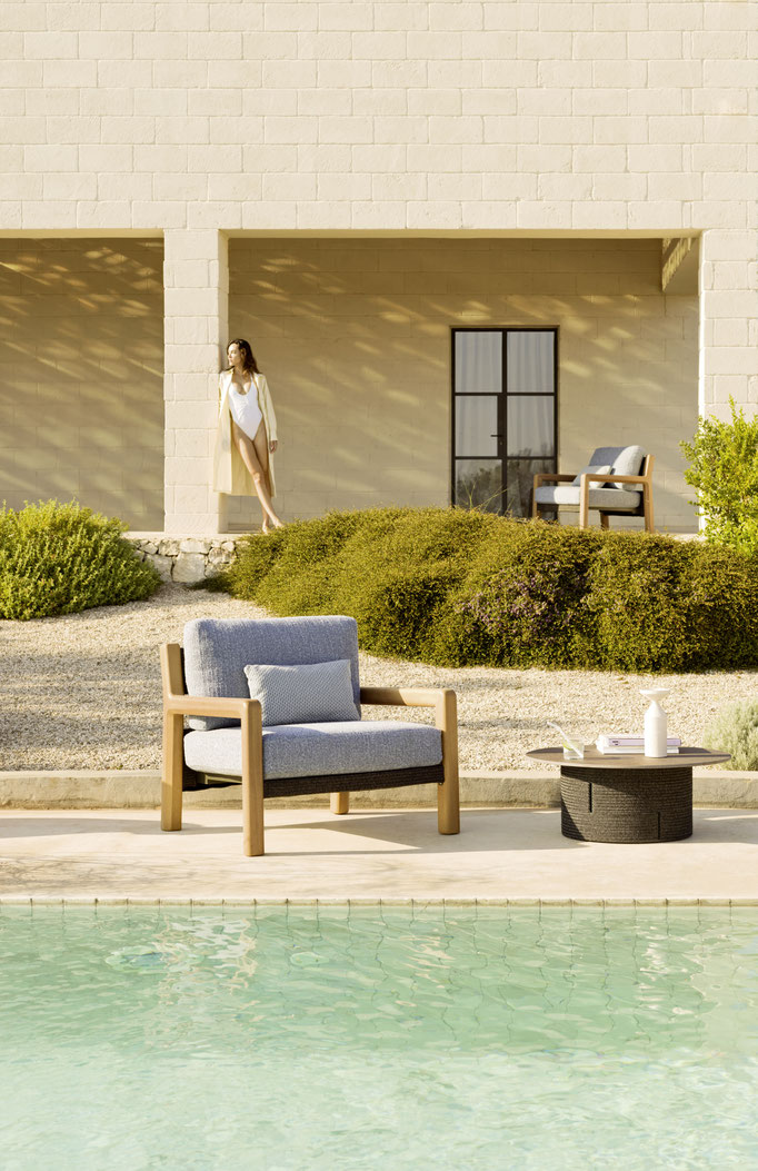 Salotto outdoor con poltrona, tavolino e piscina davanti ad architettura mediterranea.
