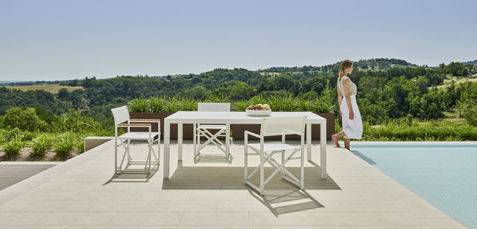 Tavolo da esterno con sedie outdoor in ambiente minimal con sfondo verde e atmosfera raffinata.