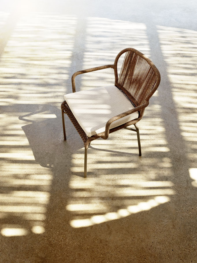 Poltrona outdoor intrecciata con cuscino chiaro, seduta da esterno in ambiente luminoso.