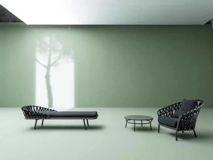 Lettino e poltrone outdoor in ambiente minimal con parete verde e tavolini da esterno.