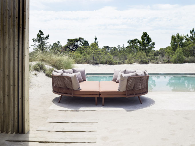 Divano outdoor intrecciato con cuscini chiari e lampada orientabile per zona relax in giardino.