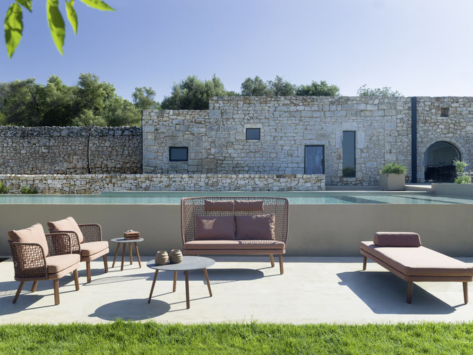 Tavolo alto outdoor con sgabello davanti a parete in pietra, arredo da esterno per zona conviviale.