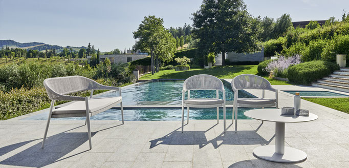 Poltrone e tavolino da esterno a bordo piscina con vista su giardino e paesaggio collinare.