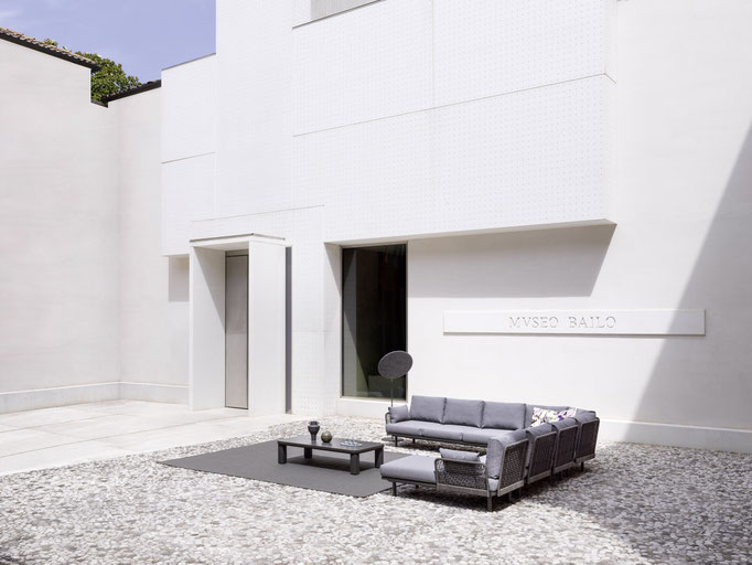 Salotto outdoor con divano e tavolino in cortile bianco minimal davanti ad architettura contemporanea.