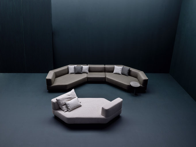 Composizione di divani modulari outdoor in ambiente scenografico con pareti scure e tavolini coordinati.