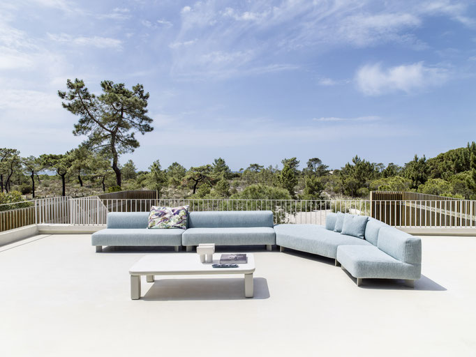 Divano modulare outdoor chiaro su terrazza panoramica con tavolino centrale e cuscini decorativi.