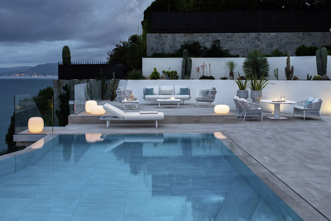 Area piscina arredata con lettini, sedute lounge e lampade da esterno per spazio outdoor elegante.
