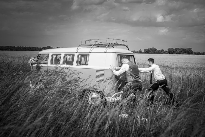 Bräutigam schiebt mit Freunden das Hochzeitsauto
