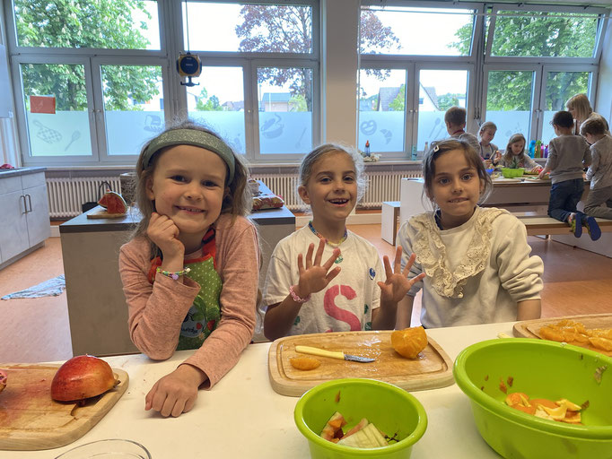 3 Mädchen schneiden begeistert Äpfel und Orangen