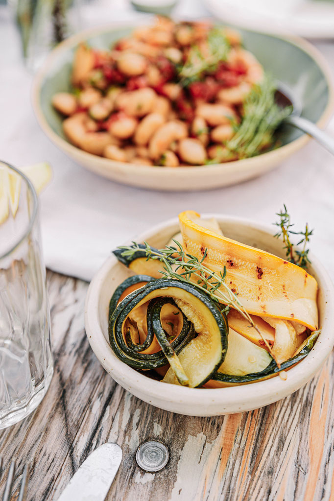 Gegrilltes Sommergemüse mit Kräutern und Zucchini auf rustikalem Holztisch. Vegane Beilage zur Garnelen-Grillparty mit regionalem Fokus.