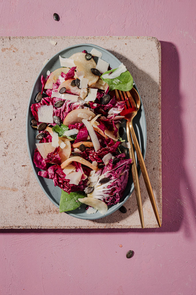 Radicchio-Salat mit fermentiertem Rettich, Kürbiskernen und Radicchio auf rosa Hintergrund – farbenfrohes Rezept aus einem Fermentationsbuch mit Fokus auf saisonale Küche.