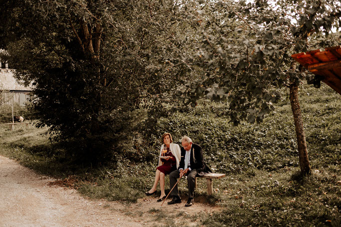Hochzeitsreportage am Wasmeier Freilichtmuseum beim Schliersee. Die ältere Generation sitzt auf einer Bank im Freien. Hochzeitsfotograf Andreas Reiter ist am Schliersee.