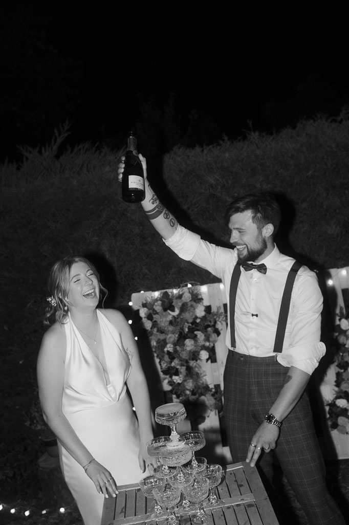 Bräutigam jubelt mit einer Flasche neben dem Champagnerturm