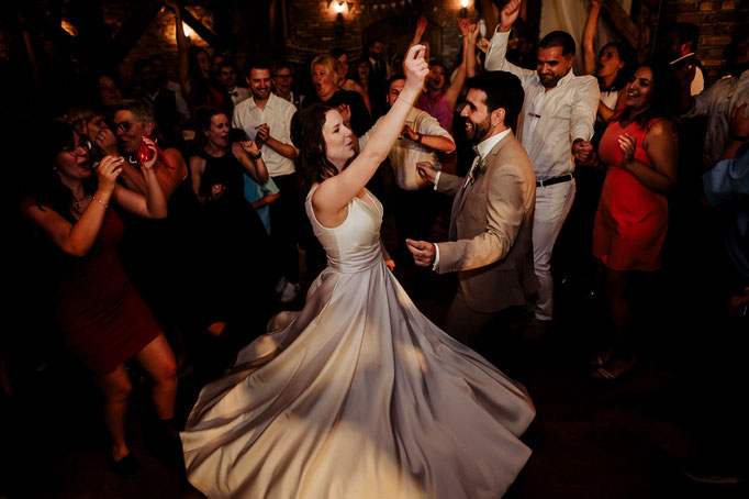 Die Hochzeitsgesellschaft tanzt und klatscht, das Brautpaar ist in der Mittte und das Brautkleid schwingt.
