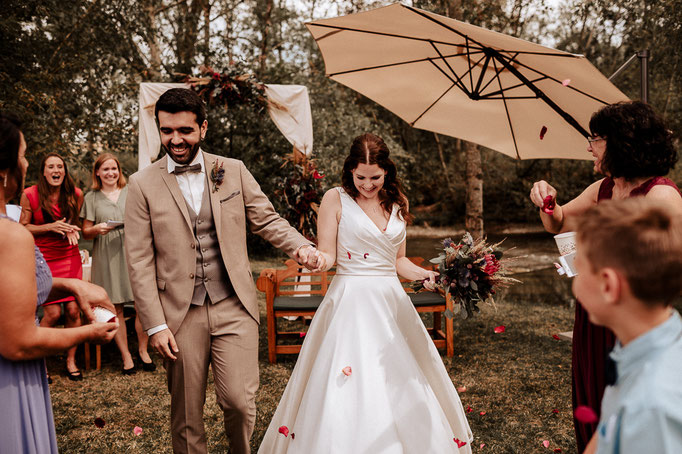 Das Brautpaar geht zwischen den Hochzeitsgästen durch und wird mit Rosenblüten beworfen