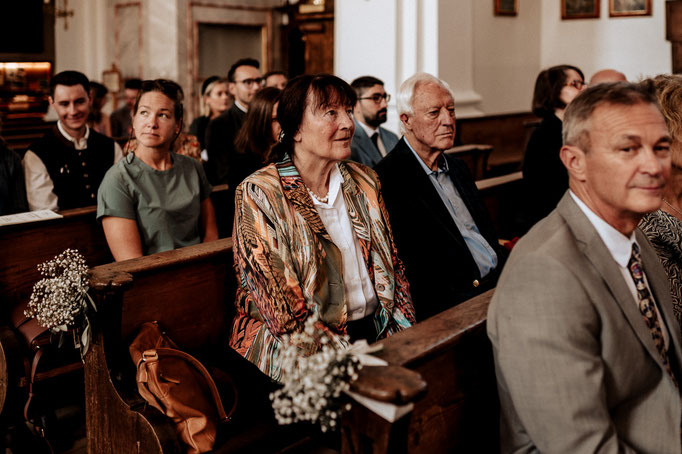Hochzeitsfotograf in der St. Sixtus Kirche am Schliersee. Die Hochzeitsgesellschaft hört der Predigt gespannt zu.