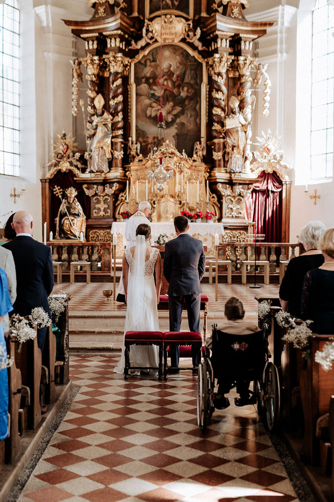 Hochzeit in der St. Sixtus Kirche am Schliersee. Hochzeitsfotograf Schliersee. Das Brautpaar steht vor dem Altar.