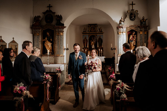 Das Brautpaar geht aus der Kapelle zwischen den Hochzeitsgästen durch.