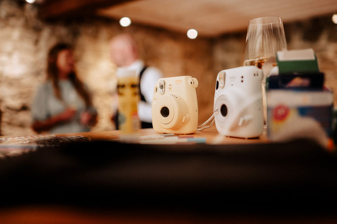 Hochzeitsreportage am Wasmeier Freilichtmuseum beim Schliersee. Es stehen Sofortbildkameras auf einem Tisch.
